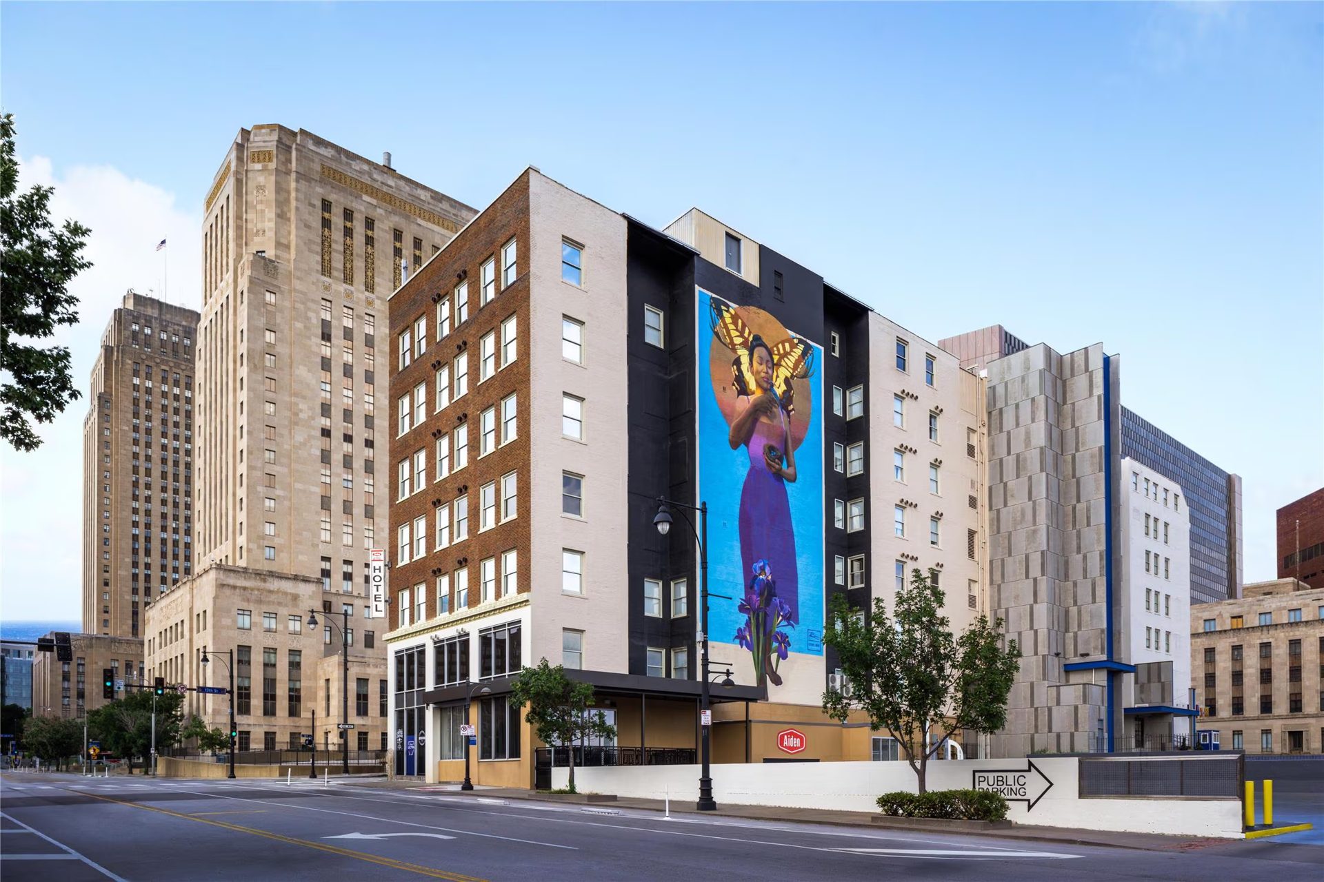 The Aiden Hotel at 13th and Oak in downtown Kansas City, with a large mural of a woman with butterfly wings painted on its side and City Hall rising behind it.